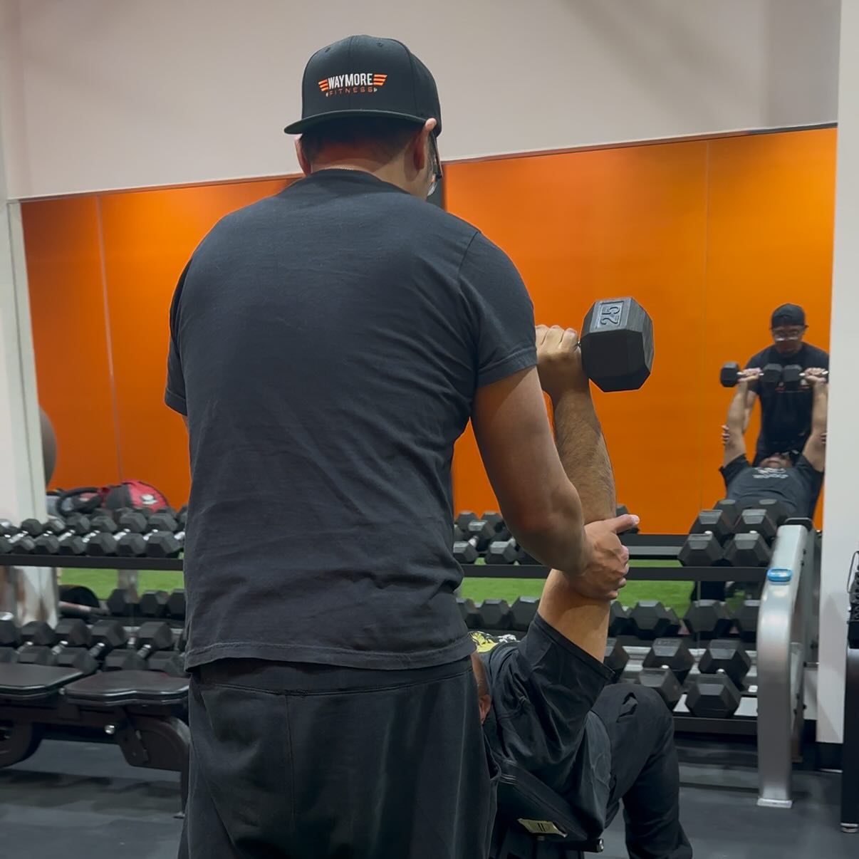 A WayMore trainer coaching a member through a seated dumbbell press in the gym