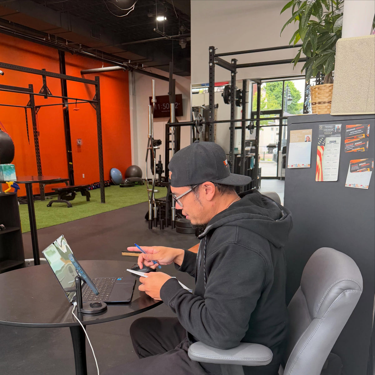 A WayMore coach working on a laptop and notebook in the orange-wall gym